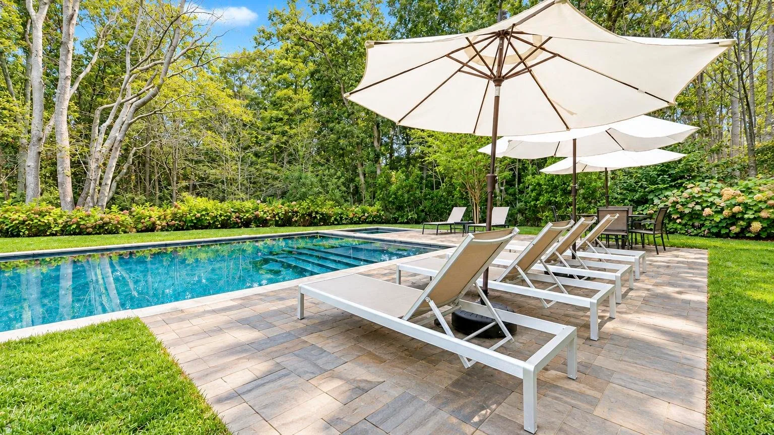 An outdoor swimming pool beside a paved deck with lounge seating and umbrellas.
