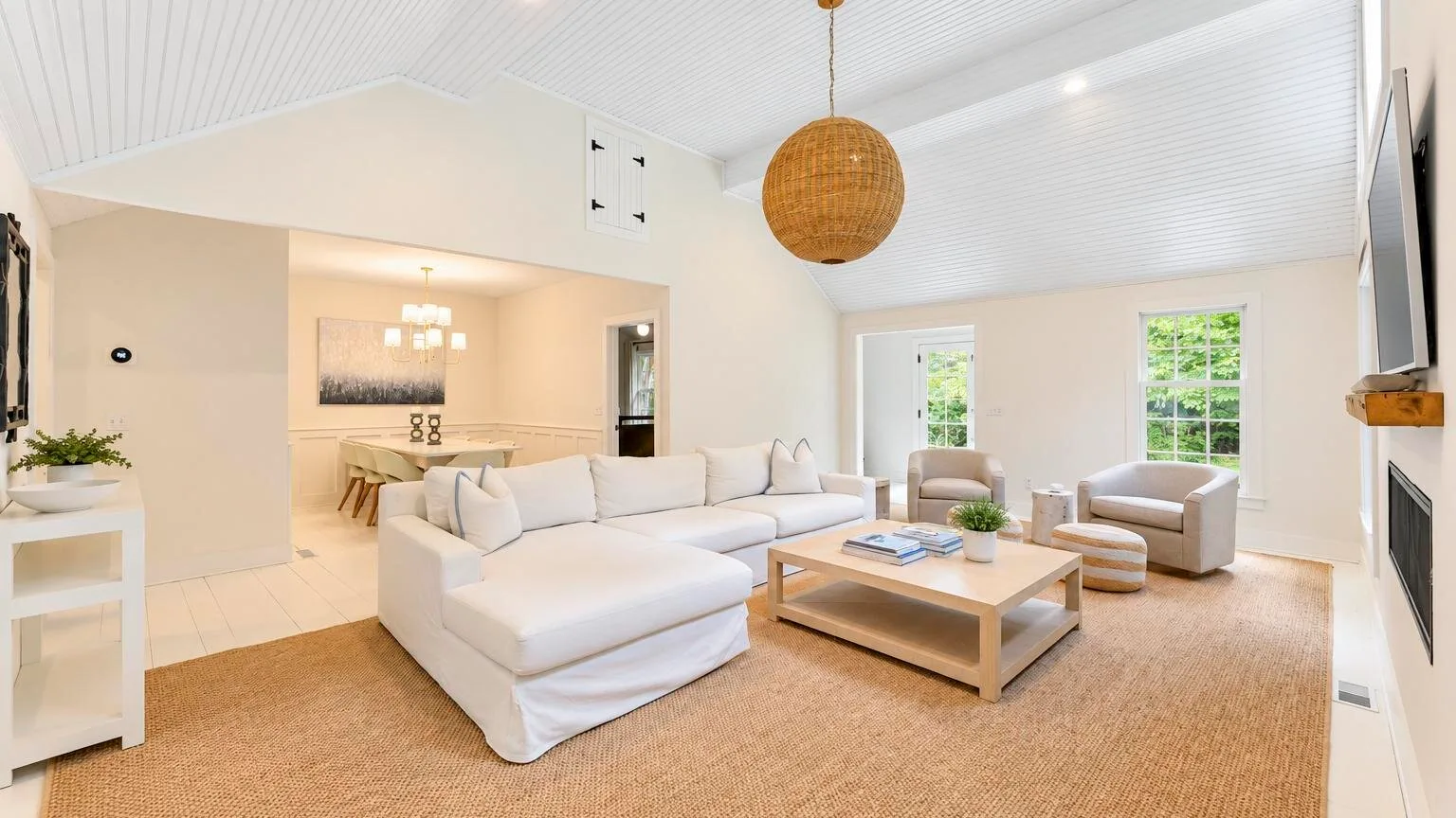 A bright living room with white seating, a coffee table, and large windows.