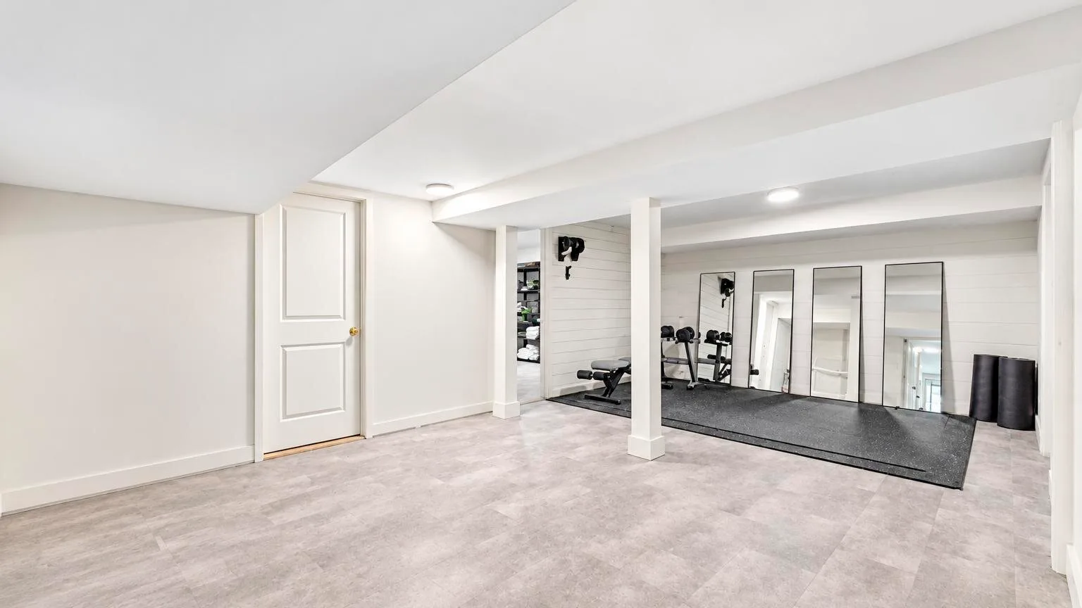 A bright basement exercise area has workout equipment and a large floor mat.