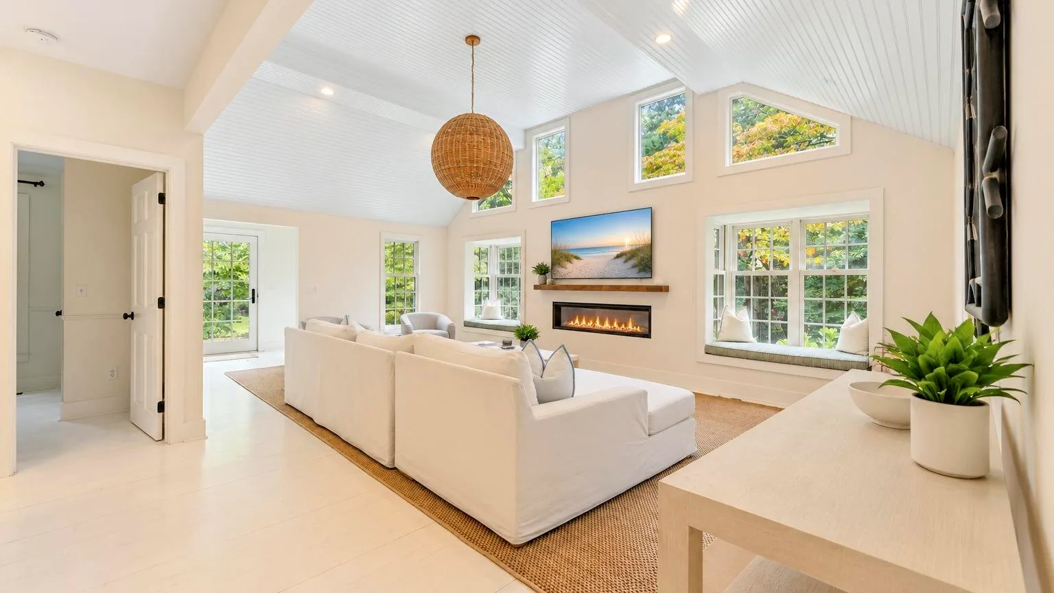 A bright living room with seating arranged around a fireplace and large windows.