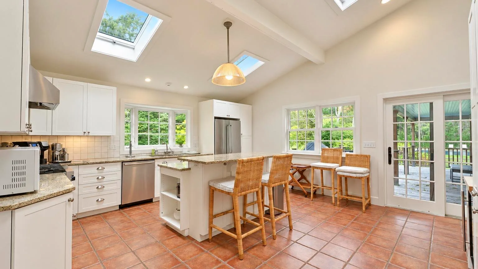 A bright kitchen with an island and dining table beneath skylights.