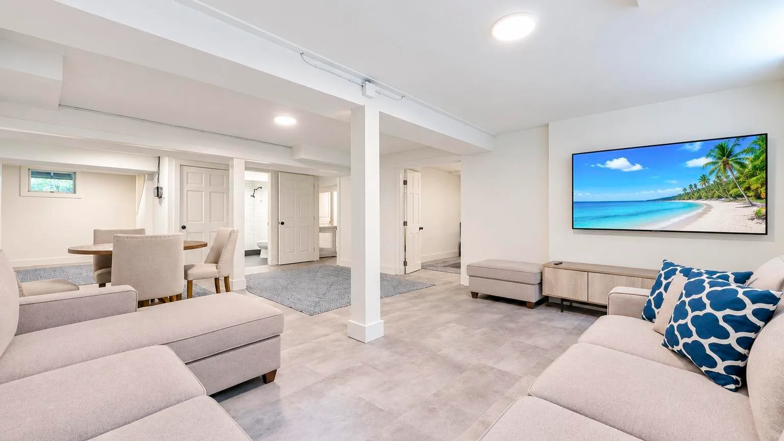 A bright living room with pale seating and a wall-mounted television.