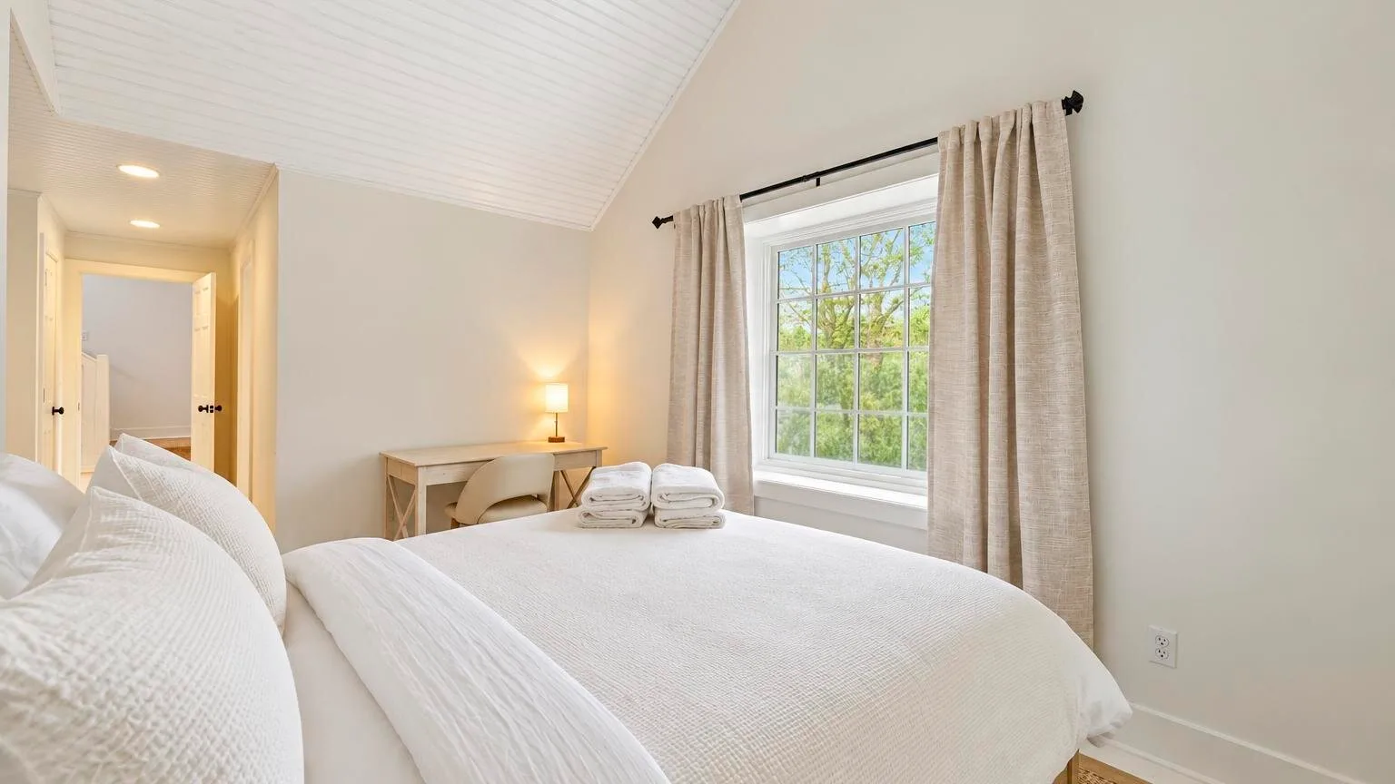 A bedroom with a neatly made bed, a window, and light curtains.