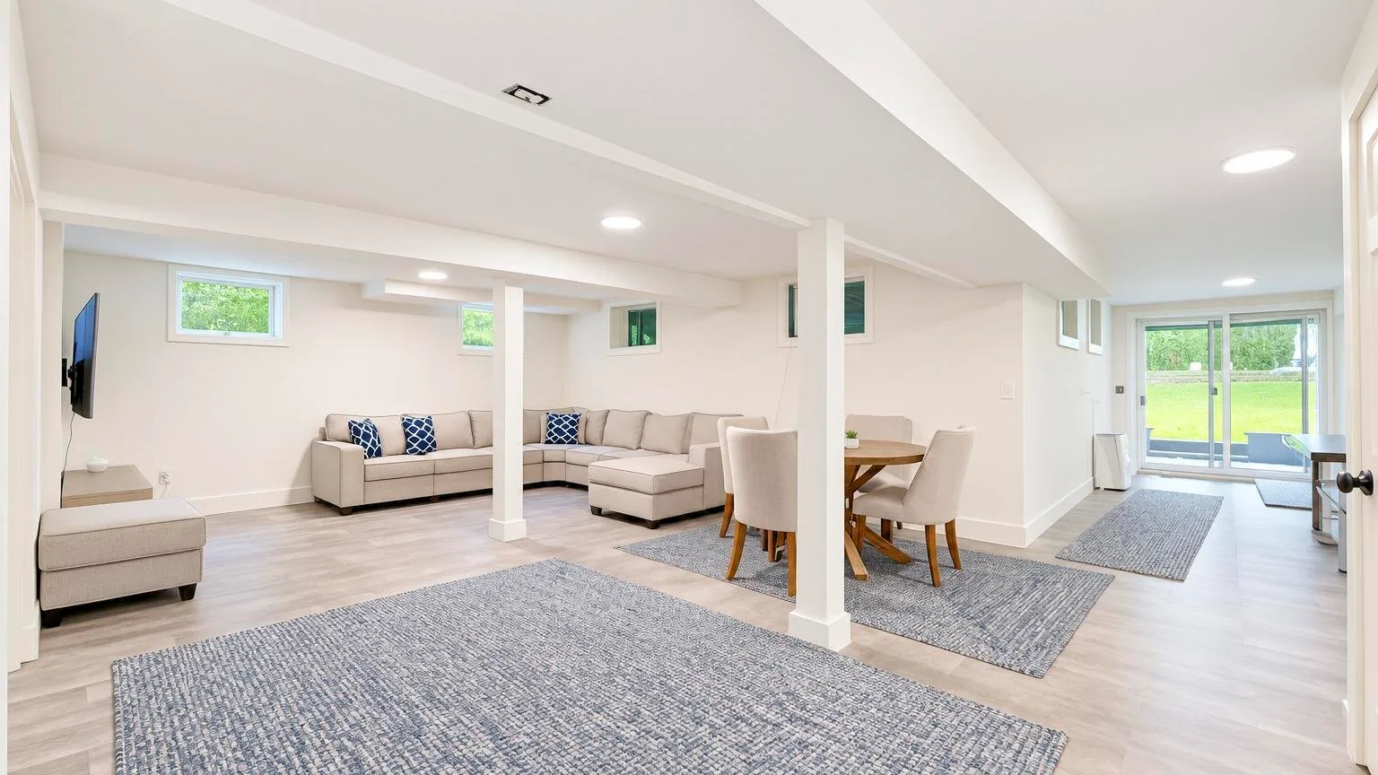 A bright basement living area with seating, a dining table, and large windows.