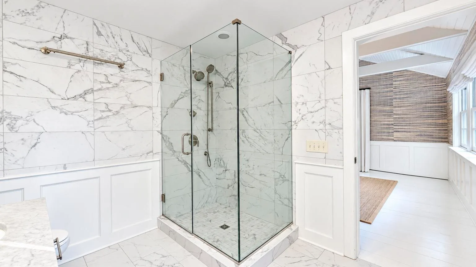 A bright bathroom with a glass shower and white marble-patterned walls.