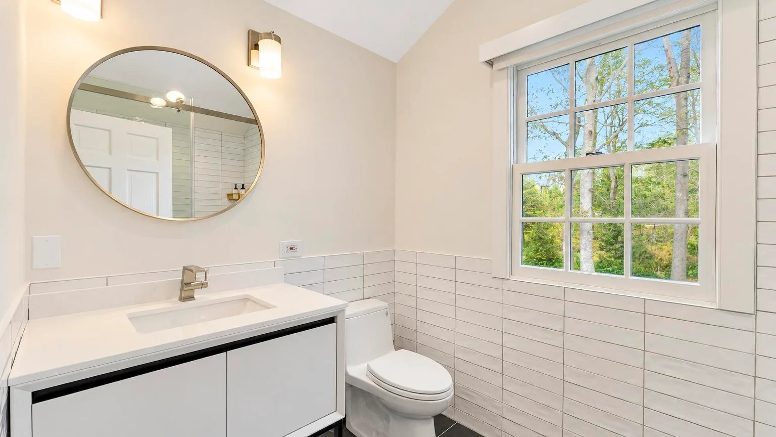 A bathroom with a vanity, round mirror, and window.