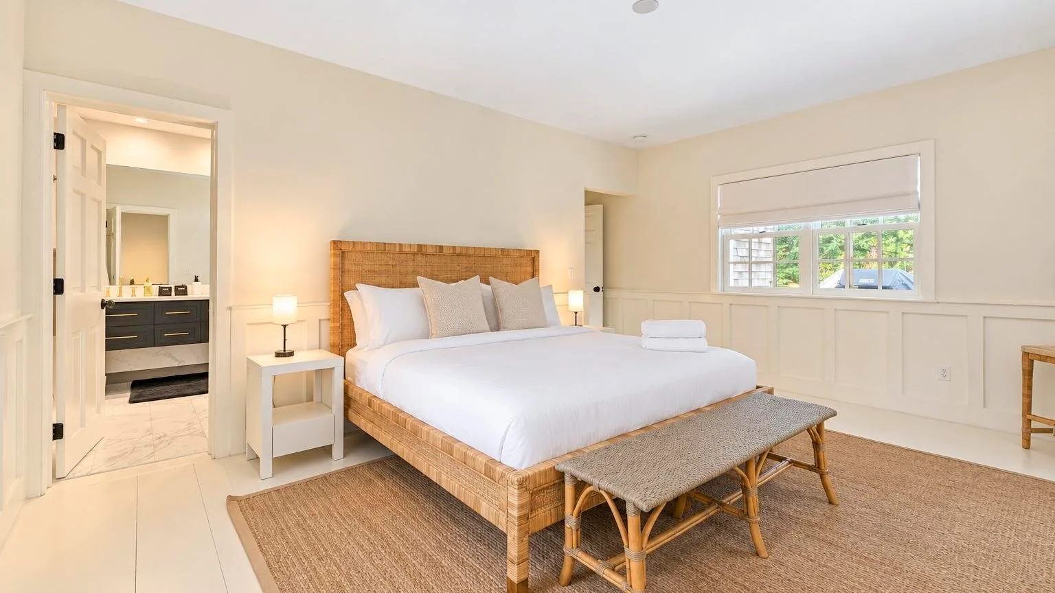 A bright bedroom with a large bed and a window overlooking greenery.