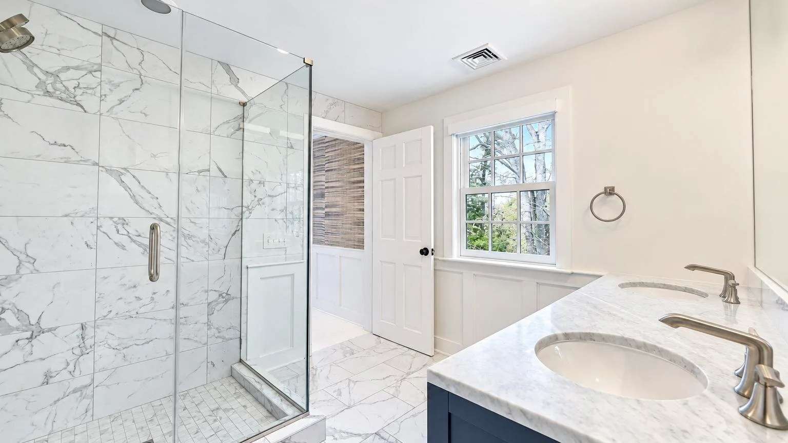 A bright bathroom with a glass shower and a sink beneath a window.