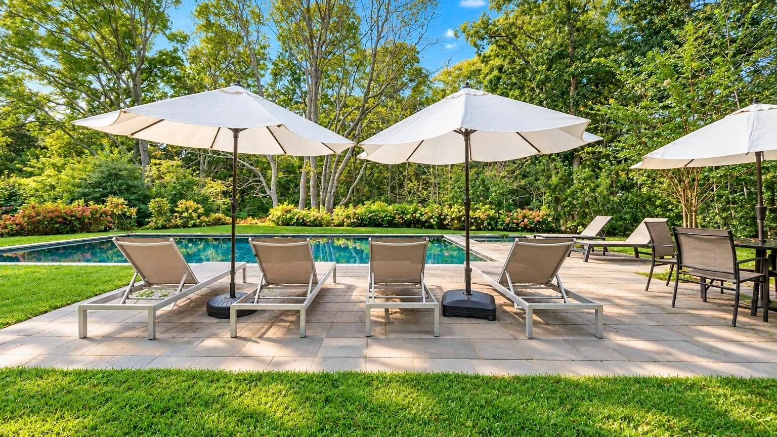 Un patio junto a una piscina al aire libre, con asientos y sombrillas.
