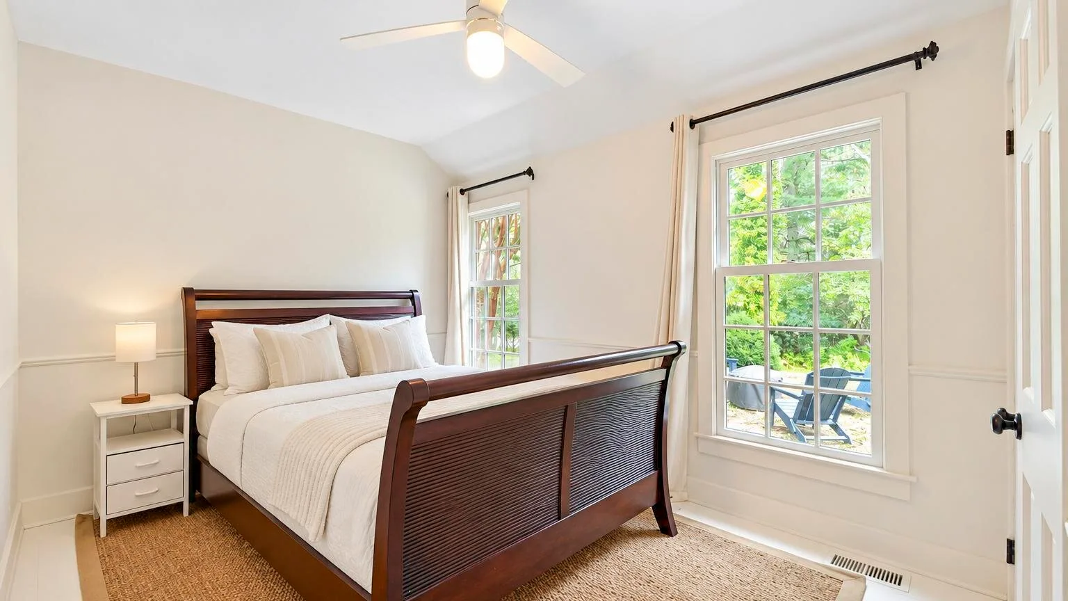 A bedroom with a bed, bedside table, and bright windows.