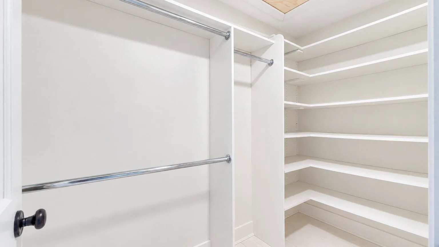 A walk-in closet with white built-in shelves and hanging rods.