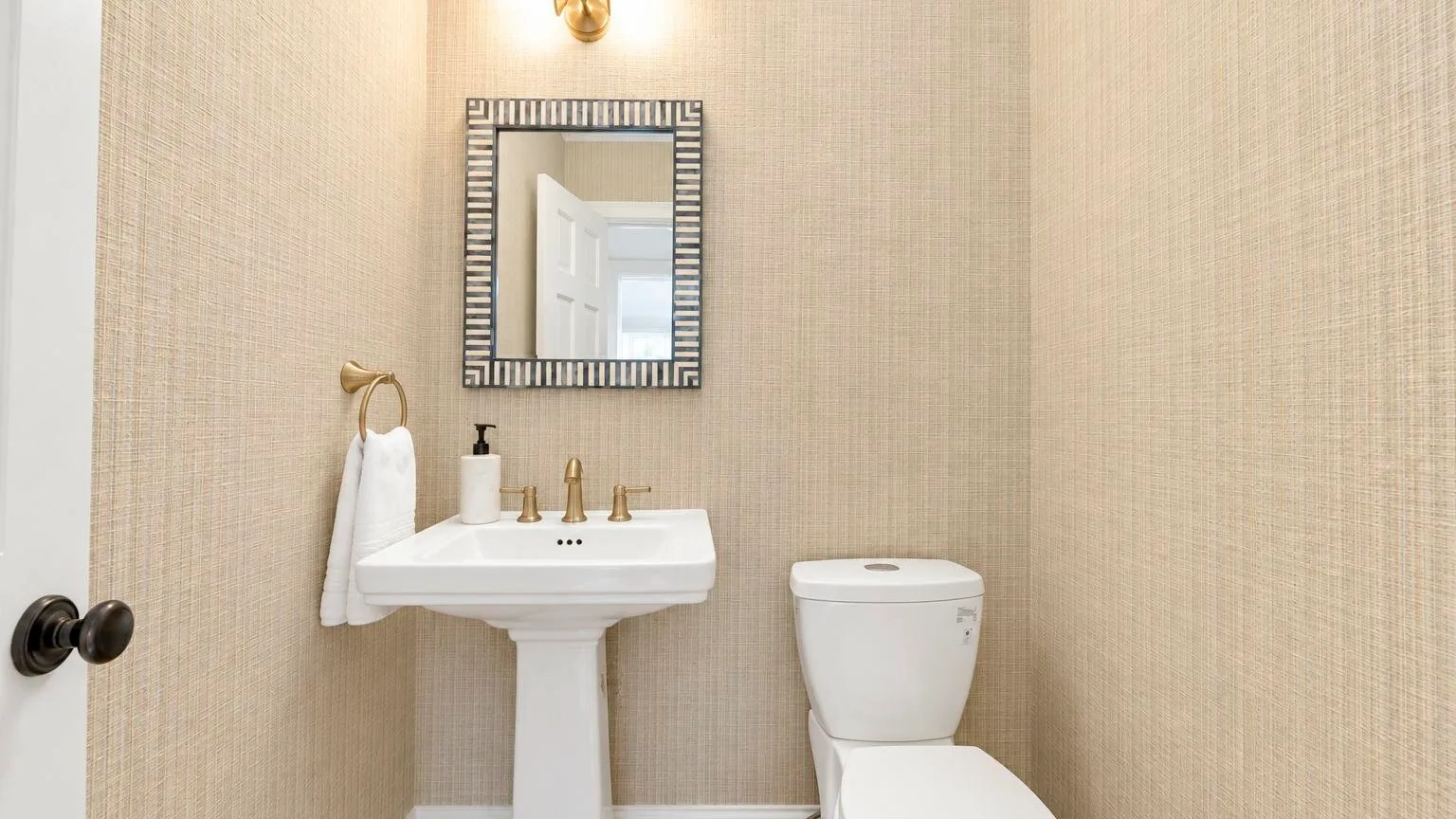 A compact bathroom with a pedestal sink, mirror, and toilet.