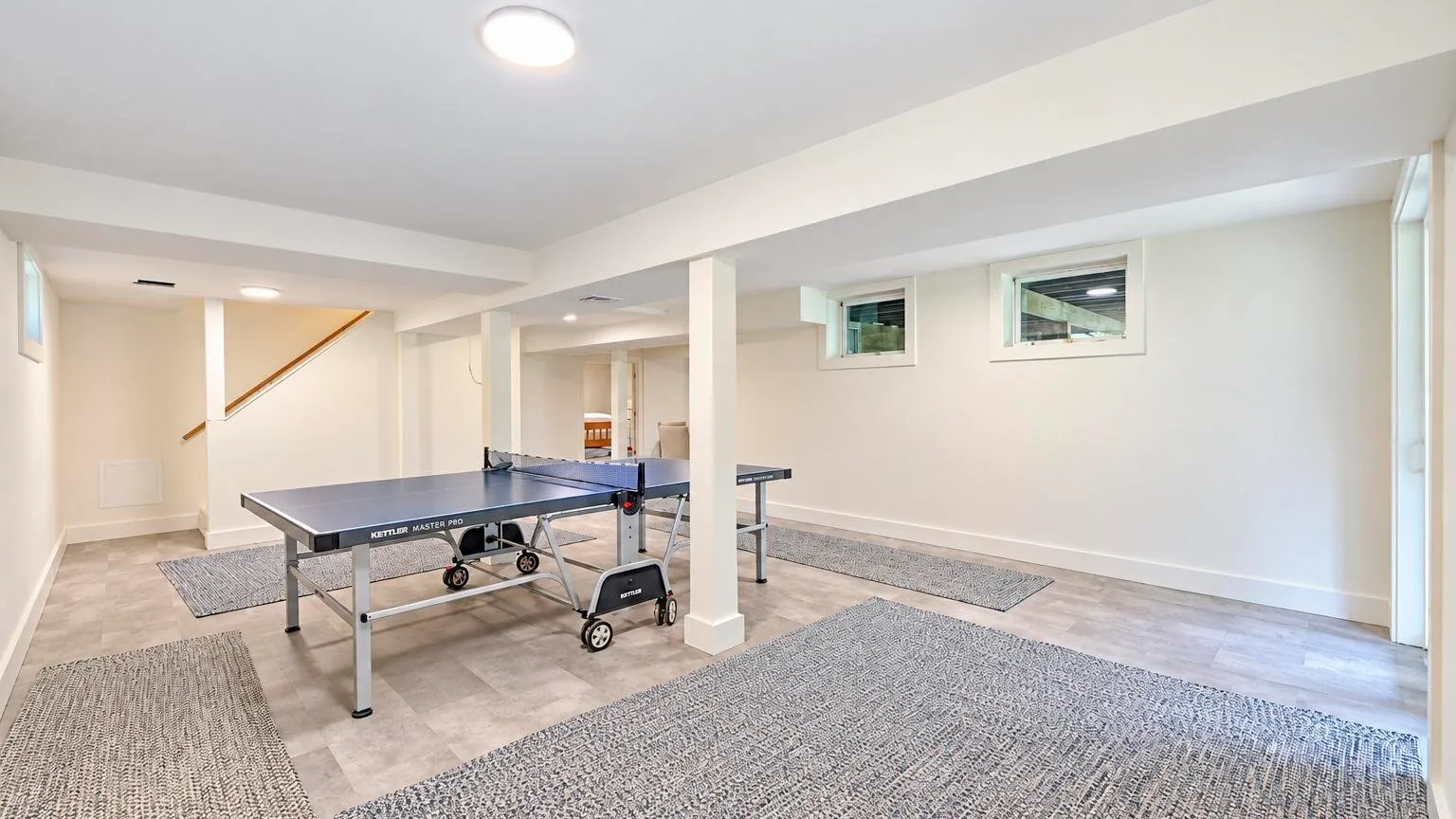 A basement recreation room with a ping-pong table and area rugs.