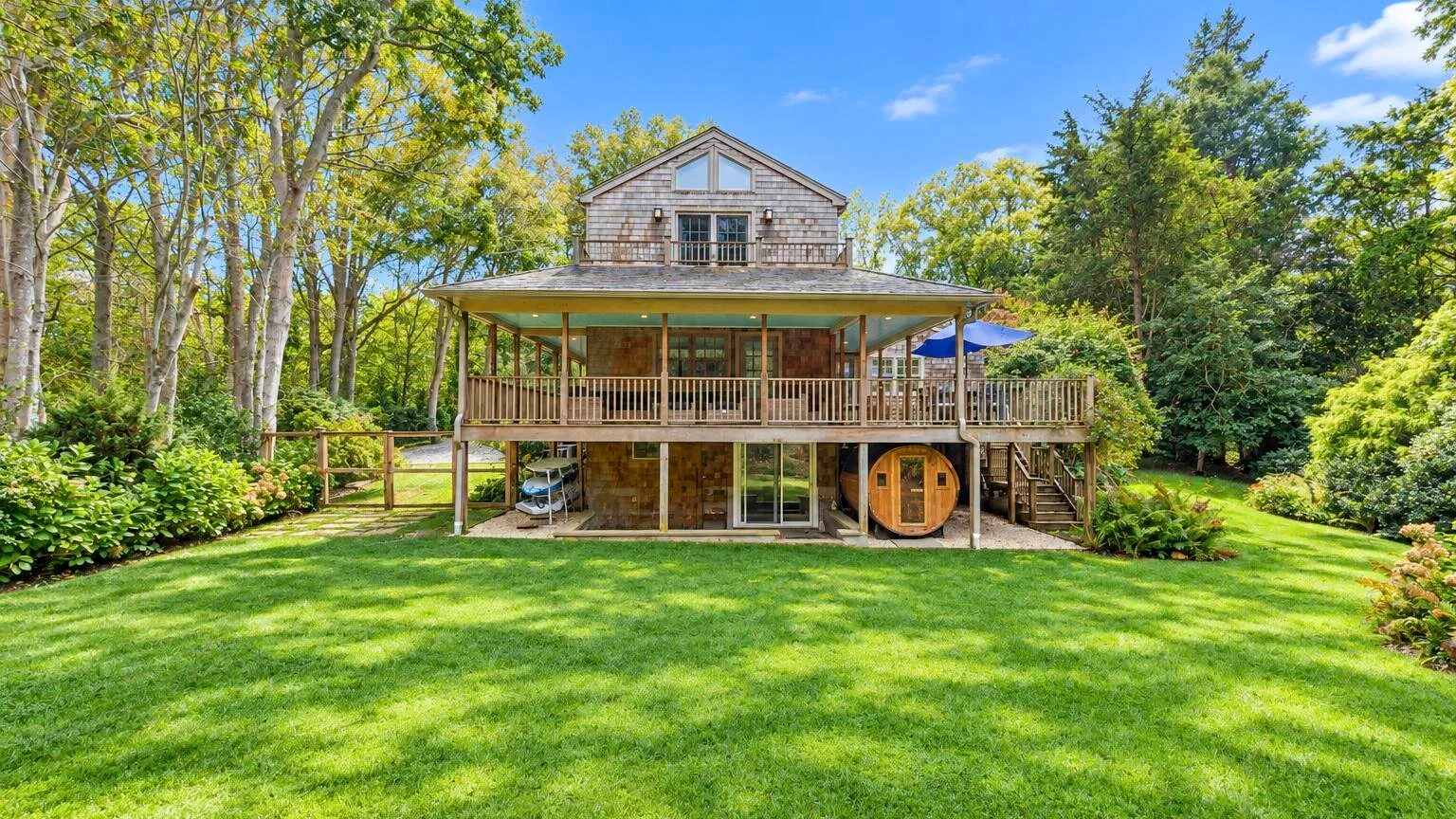 A large wooden house stands behind a broad green lawn, surrounded by trees.