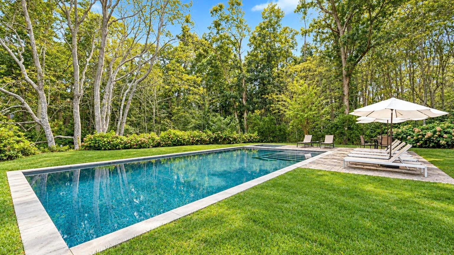 An outdoor swimming pool sits beside a green lawn and trees.