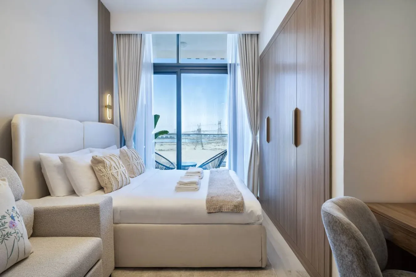 A bedroom with a bed, seating, and large windows overlooking the sea.