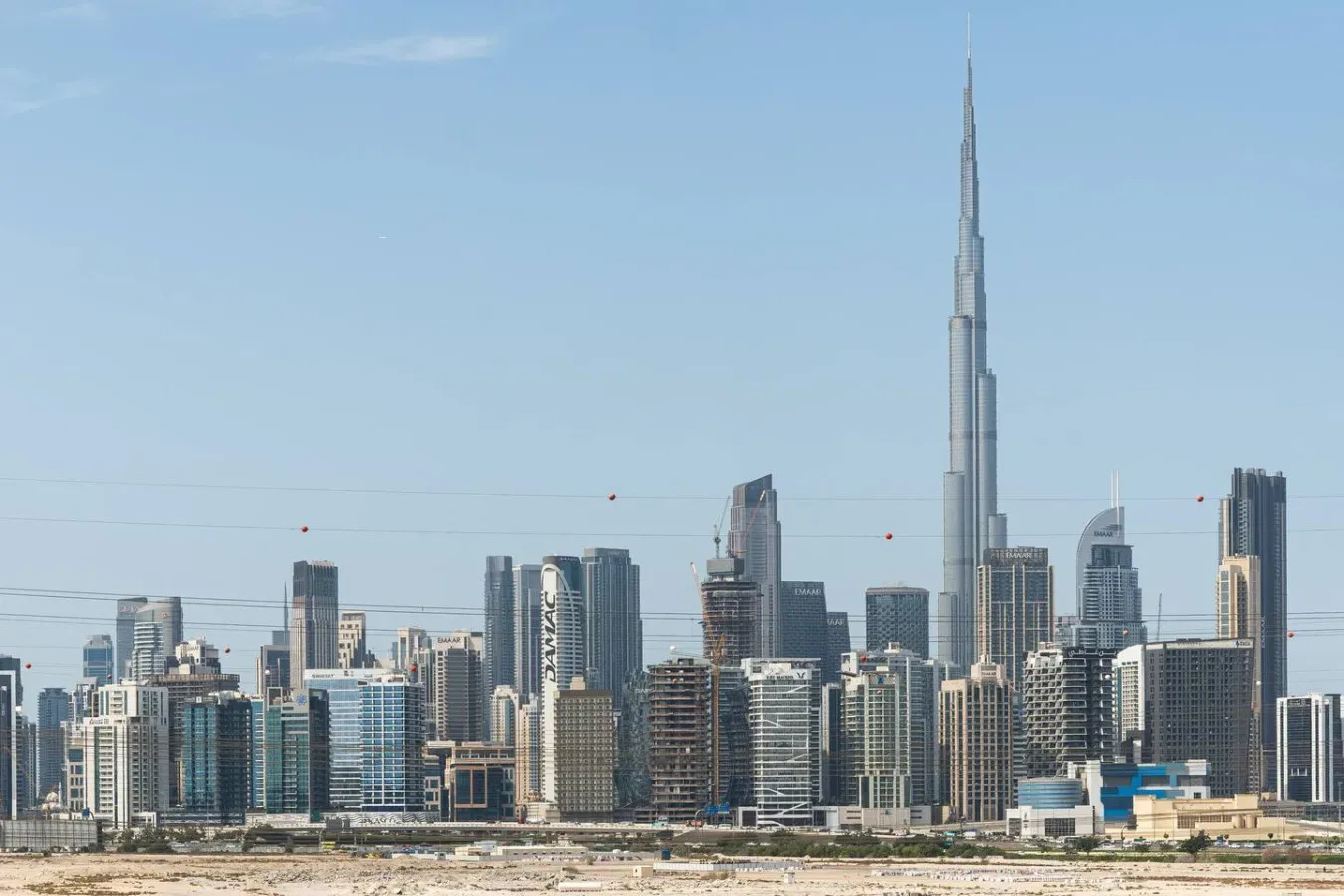 A modern city skyline rises against a clear blue sky.
