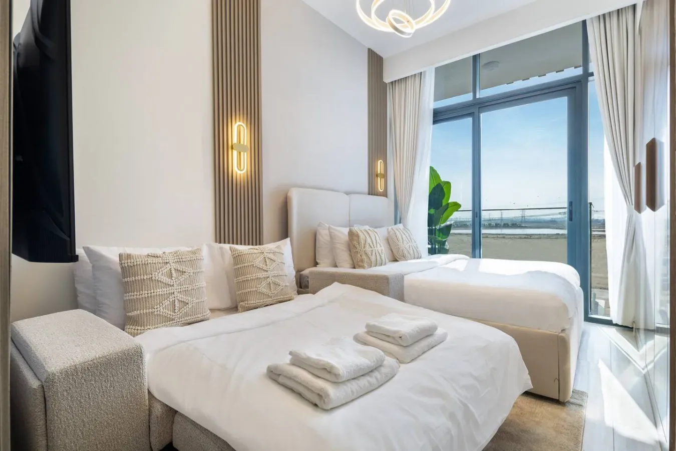 A bright bedroom with two beds, folded towels, and a large window.