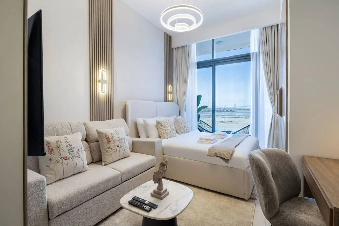 A bright bedroom with a bed, a seating area, and a large window.