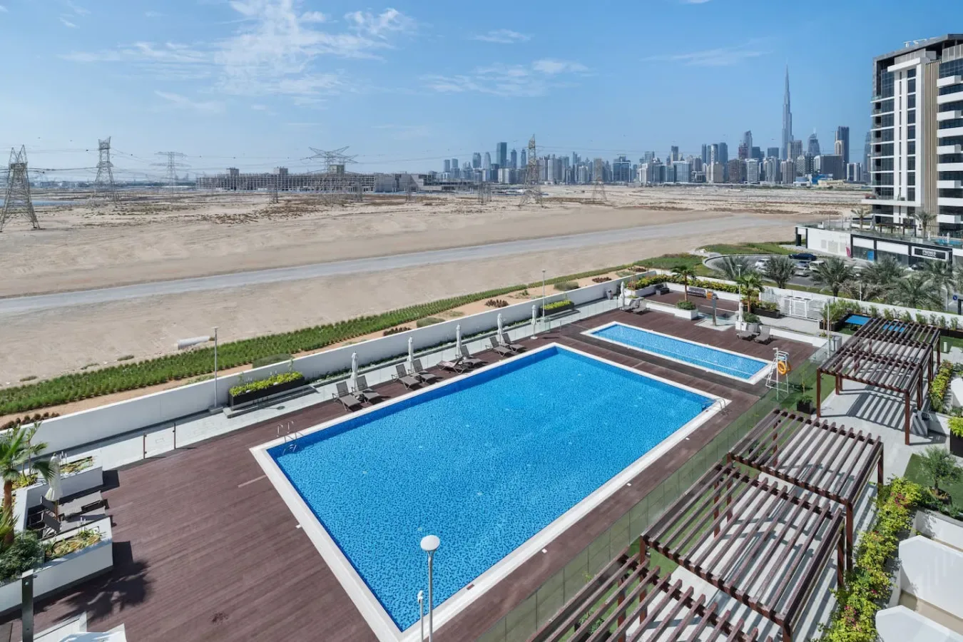 A rooftop swimming pool overlooks an open landscape and distant city skyline.