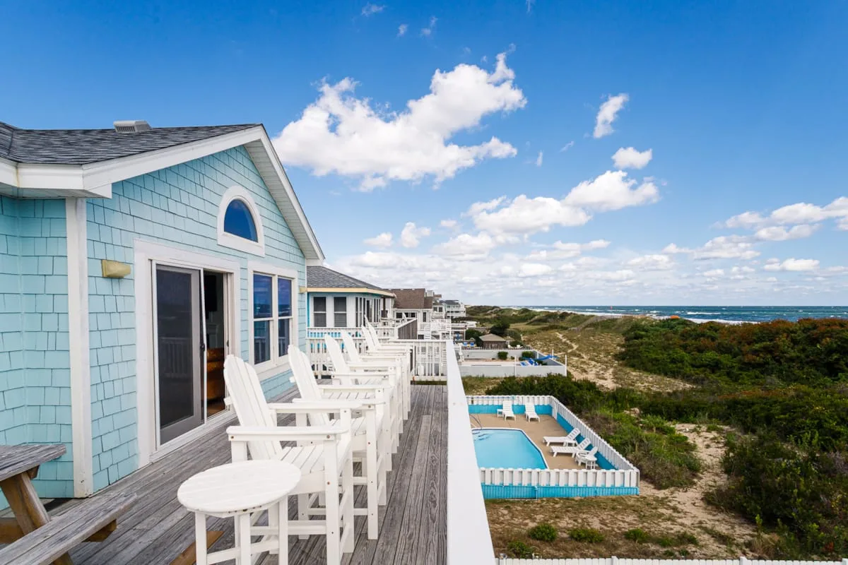 Una casa junto al mar con una terraza de madera frente a una piscina y el océano.