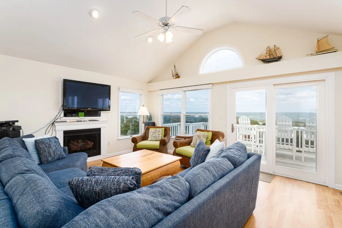 Una sala de estar con asientos azules, una chimenea y grandes ventanas con vista al agua.