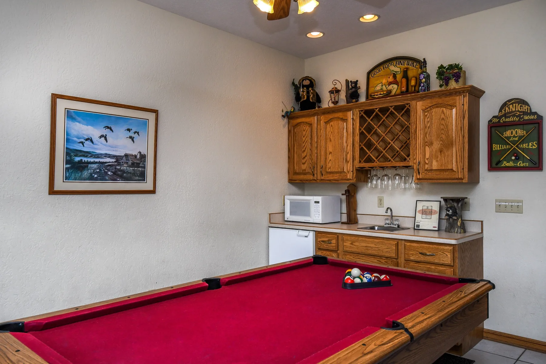 Una sala de juegos con una mesa de billar de paño rojo y una pequeña cocina.