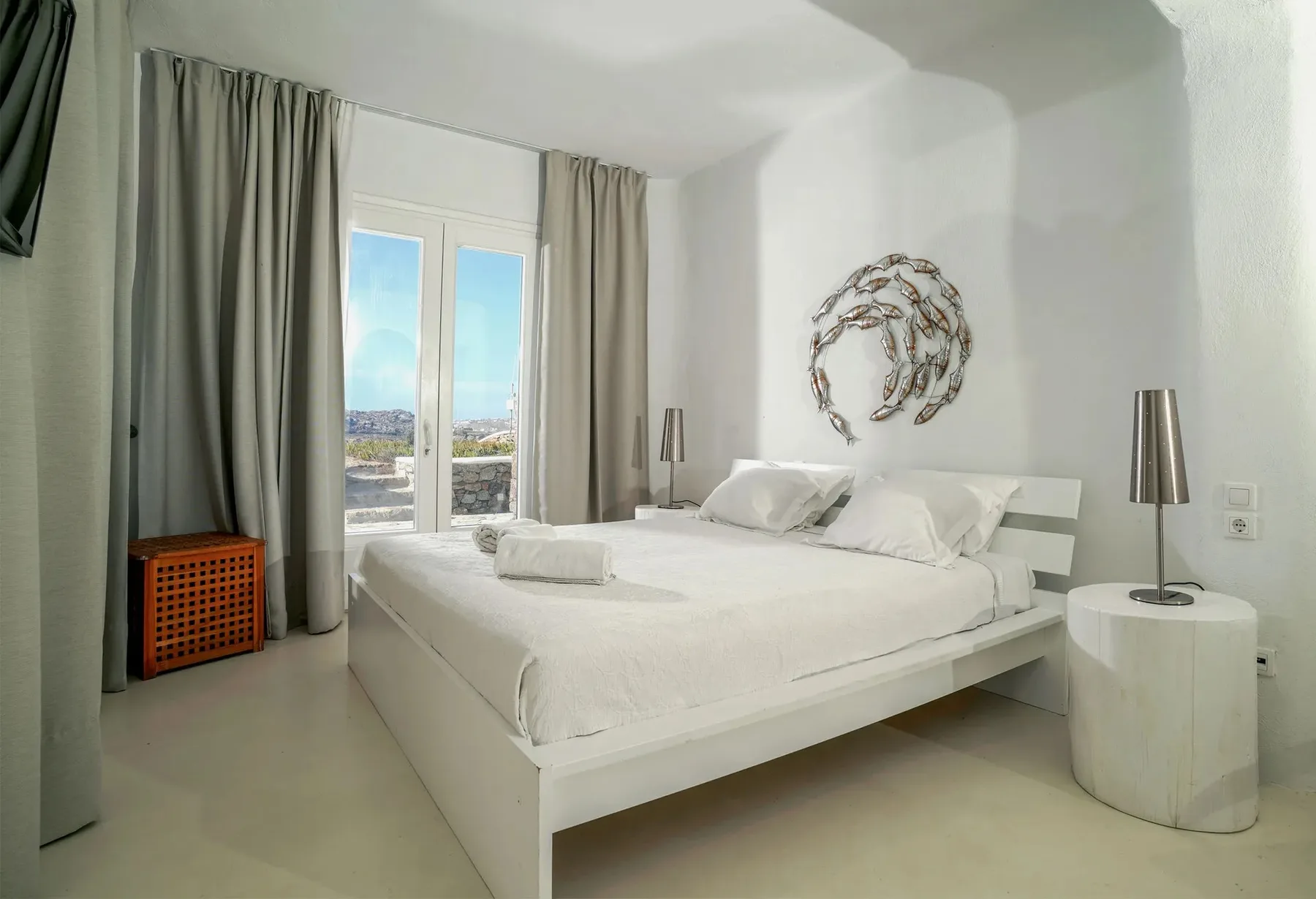 A bright bedroom with a white bed, gray curtains, and a glass door.