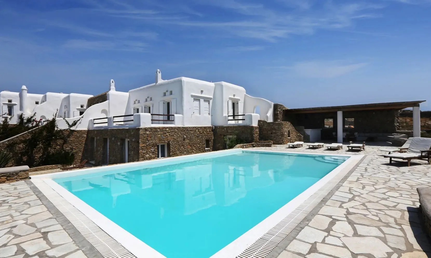 Una piscina junto a edificios blancos y un patio pavimentado.