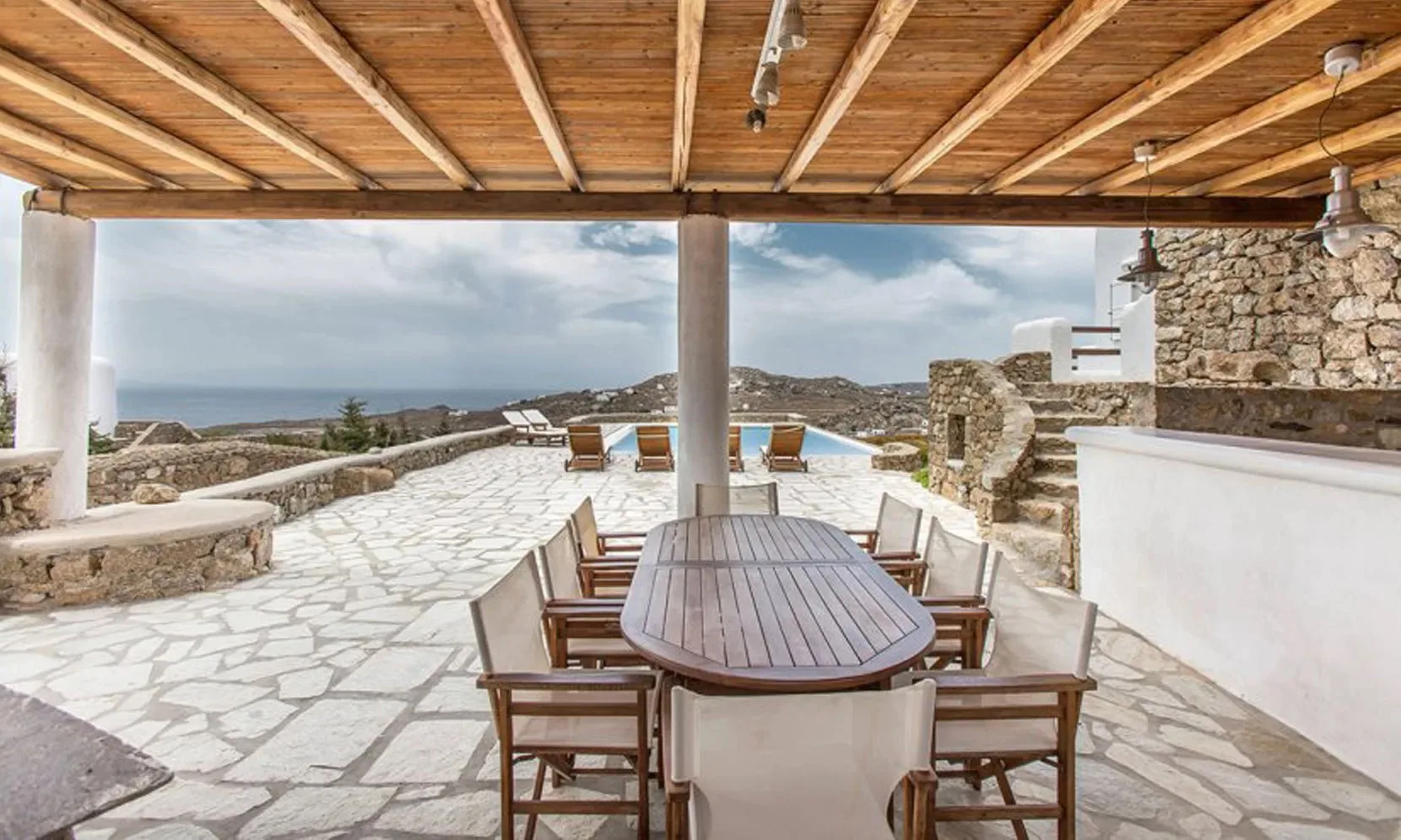Una terraza de piedra con una mesa larga y vistas al mar.