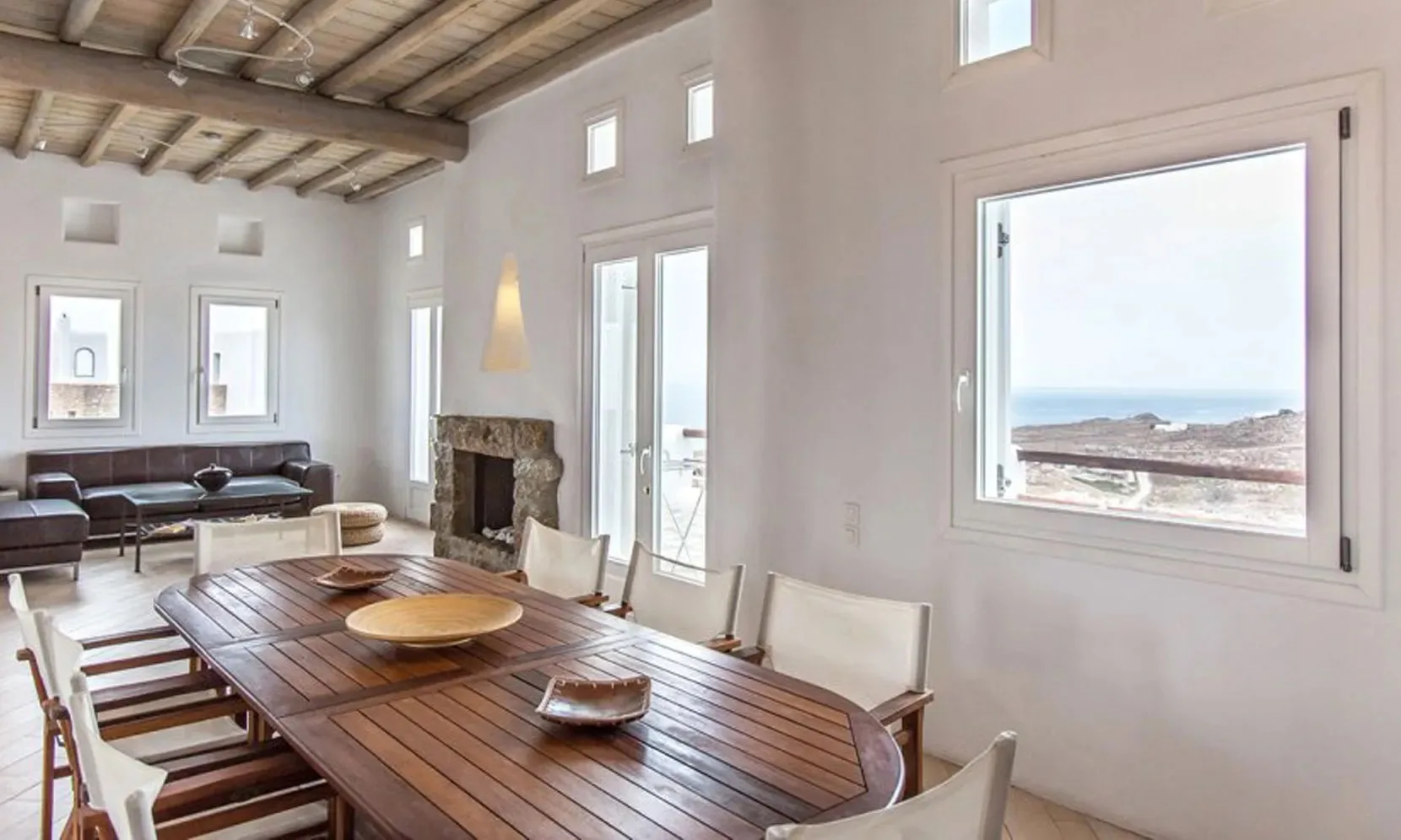 Comedor con una larga mesa de madera y ventanas con vistas al mar.