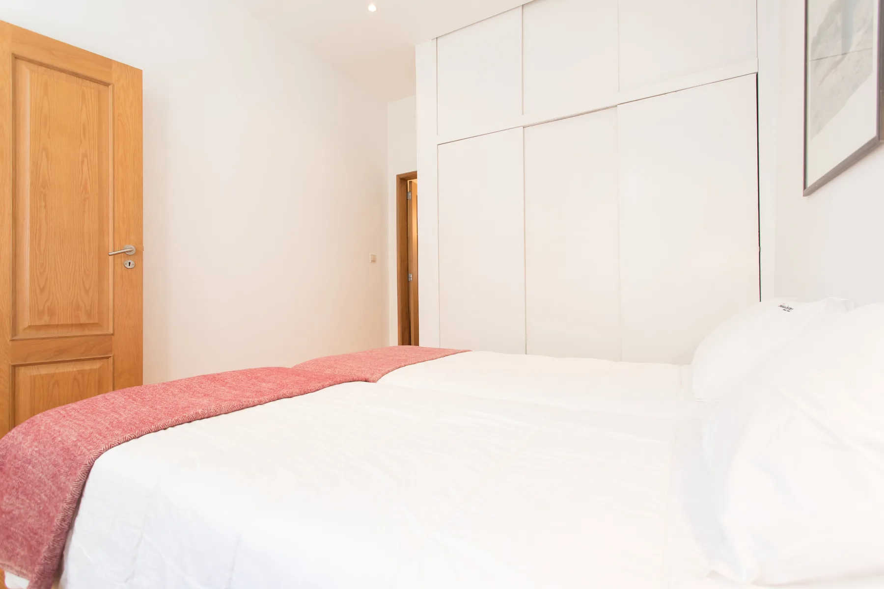 Un dormitorio con una cama cubierta de ropa de cama blanca y una manta rosa.