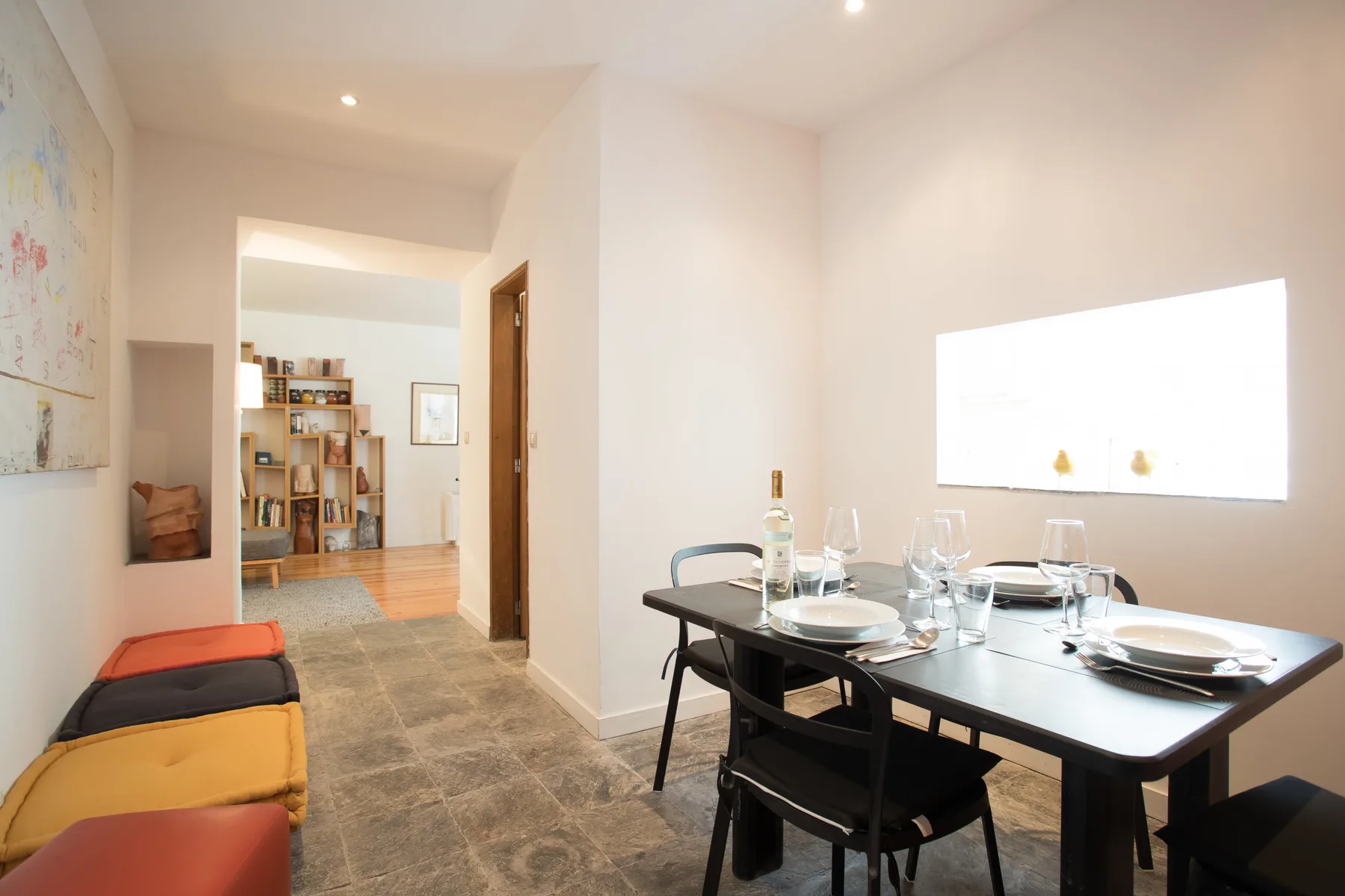 Comedor con una mesa oscura y asientos de colores junto a la pared.
