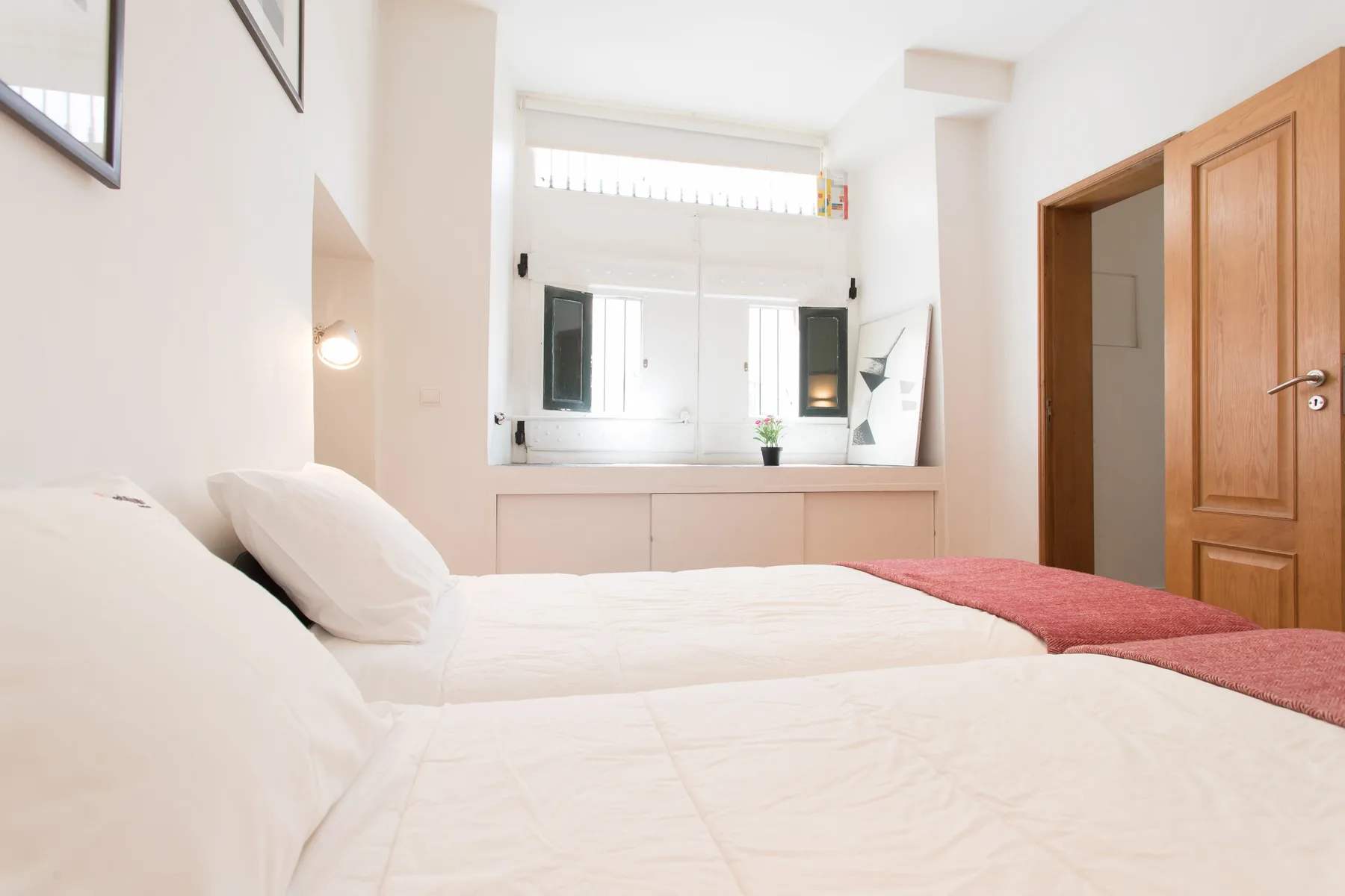 Un dormitorio luminoso con ropa de cama blanca y una manta roja sobre la cama.