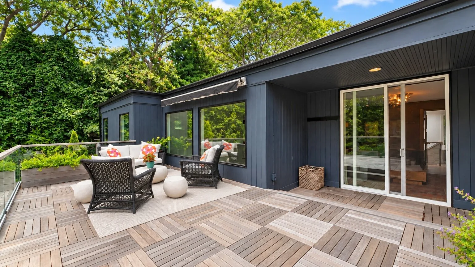 A modern home opens onto a spacious wooden deck surrounded by greenery.