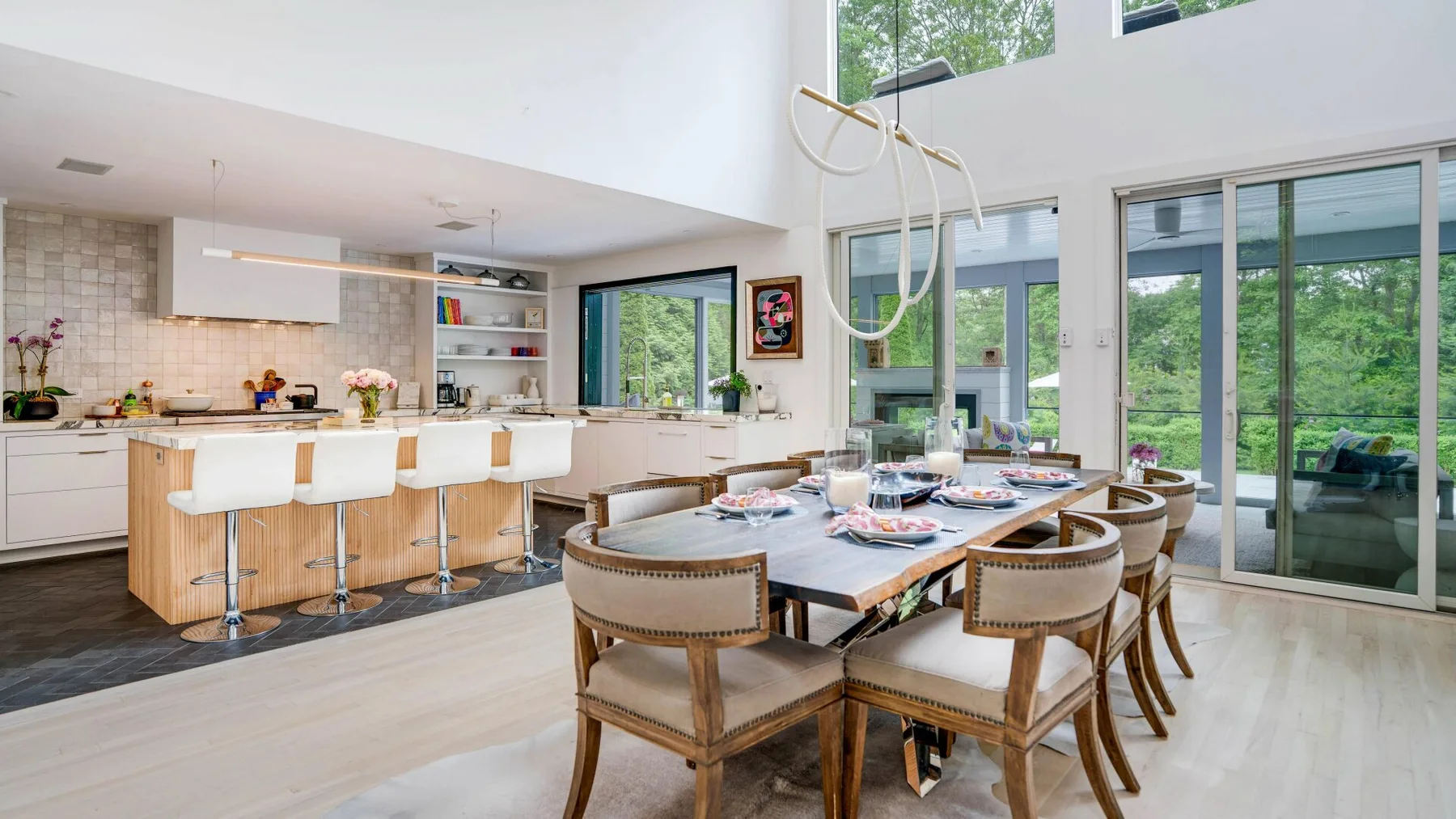 An open-plan dining area and kitchen with a long table beside large windows.