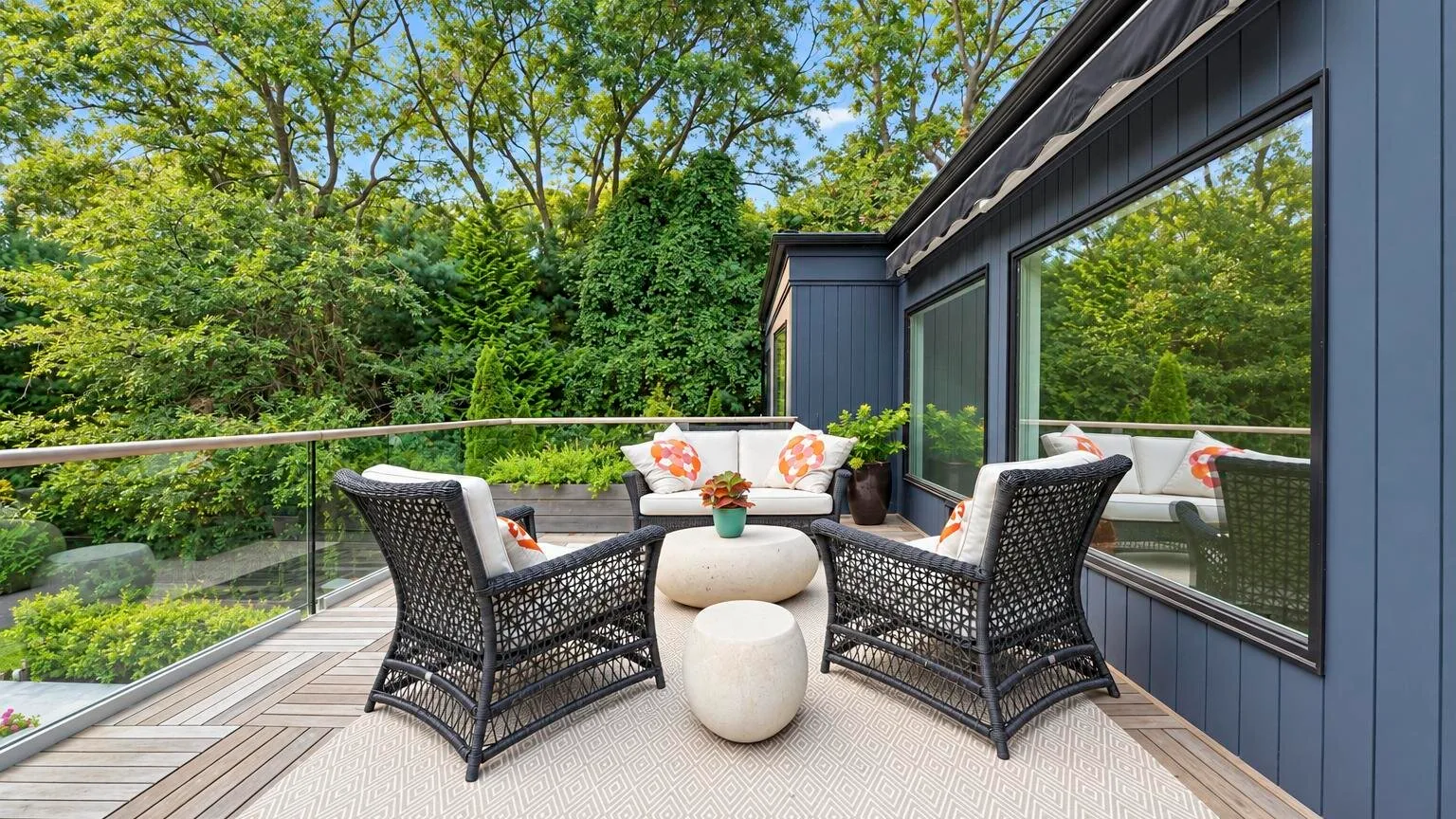An outdoor patio seating area has woven chairs, a small table, and glass railing.