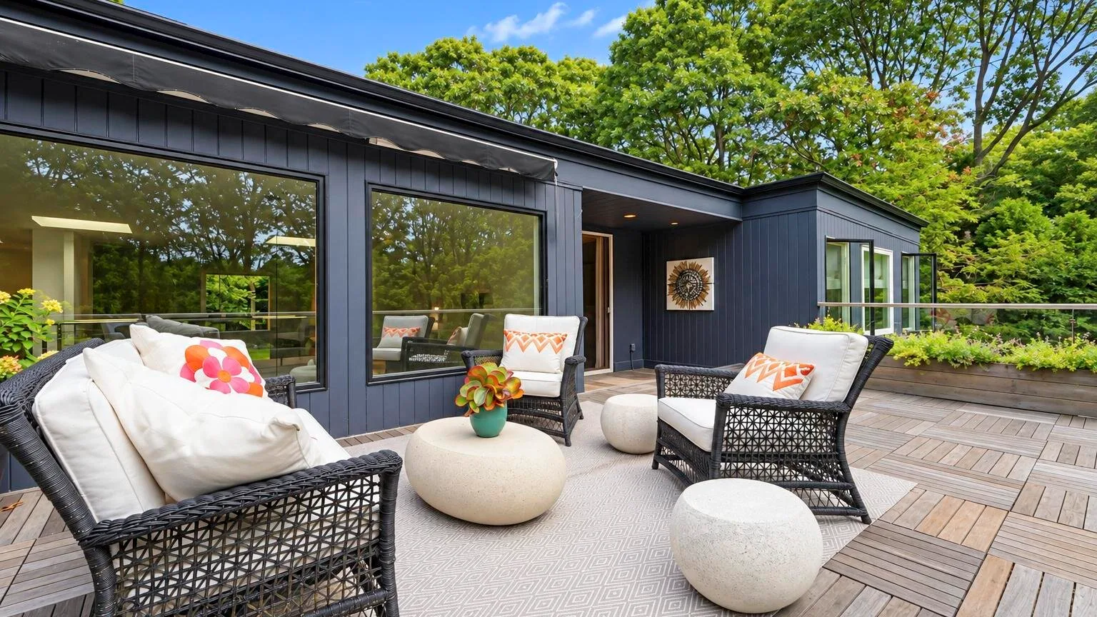 A modern house opens onto a patio with outdoor seating and leafy trees.