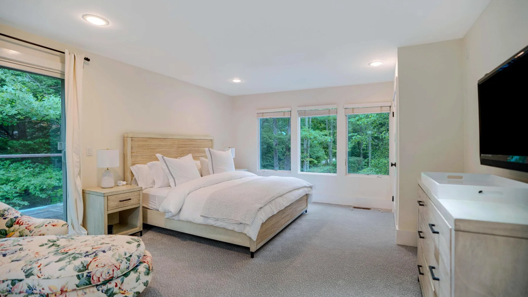 A bright bedroom with a large bed and windows overlooking greenery.
