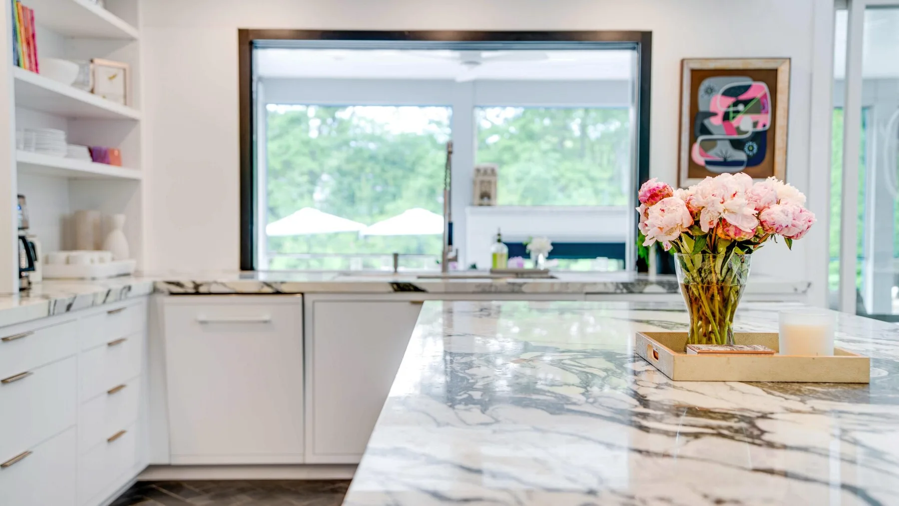 A bright white kitchen with a marble island and a large window.
