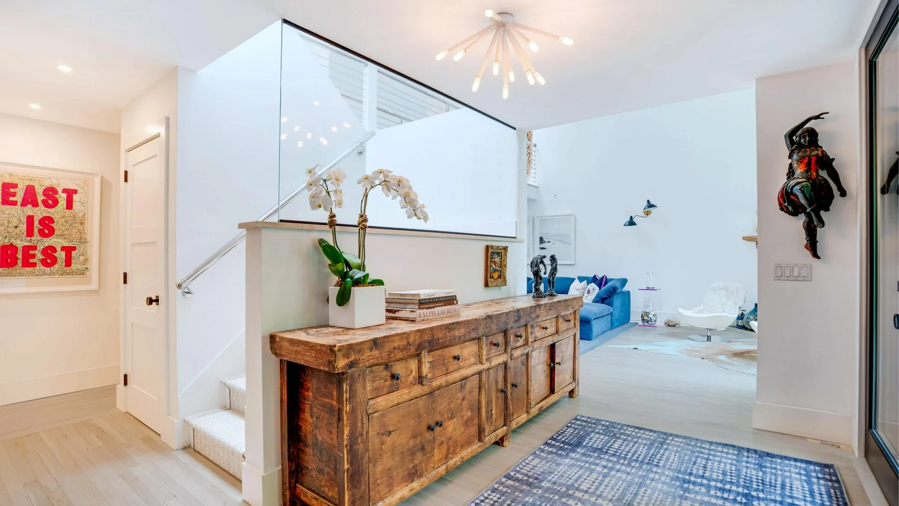 A bright open-plan living area with a wooden sideboard and blue seating.