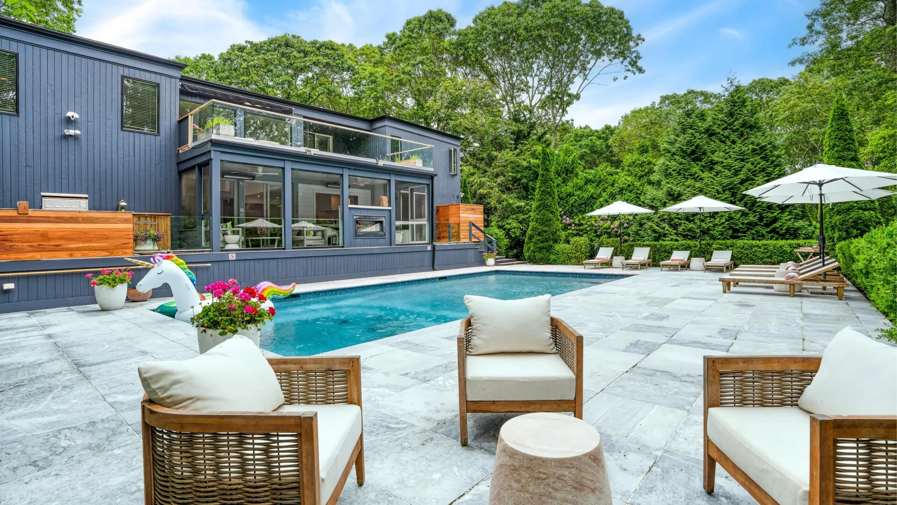Una casa moderna da a una piscina y a un amplio patio con asientos al aire libre.