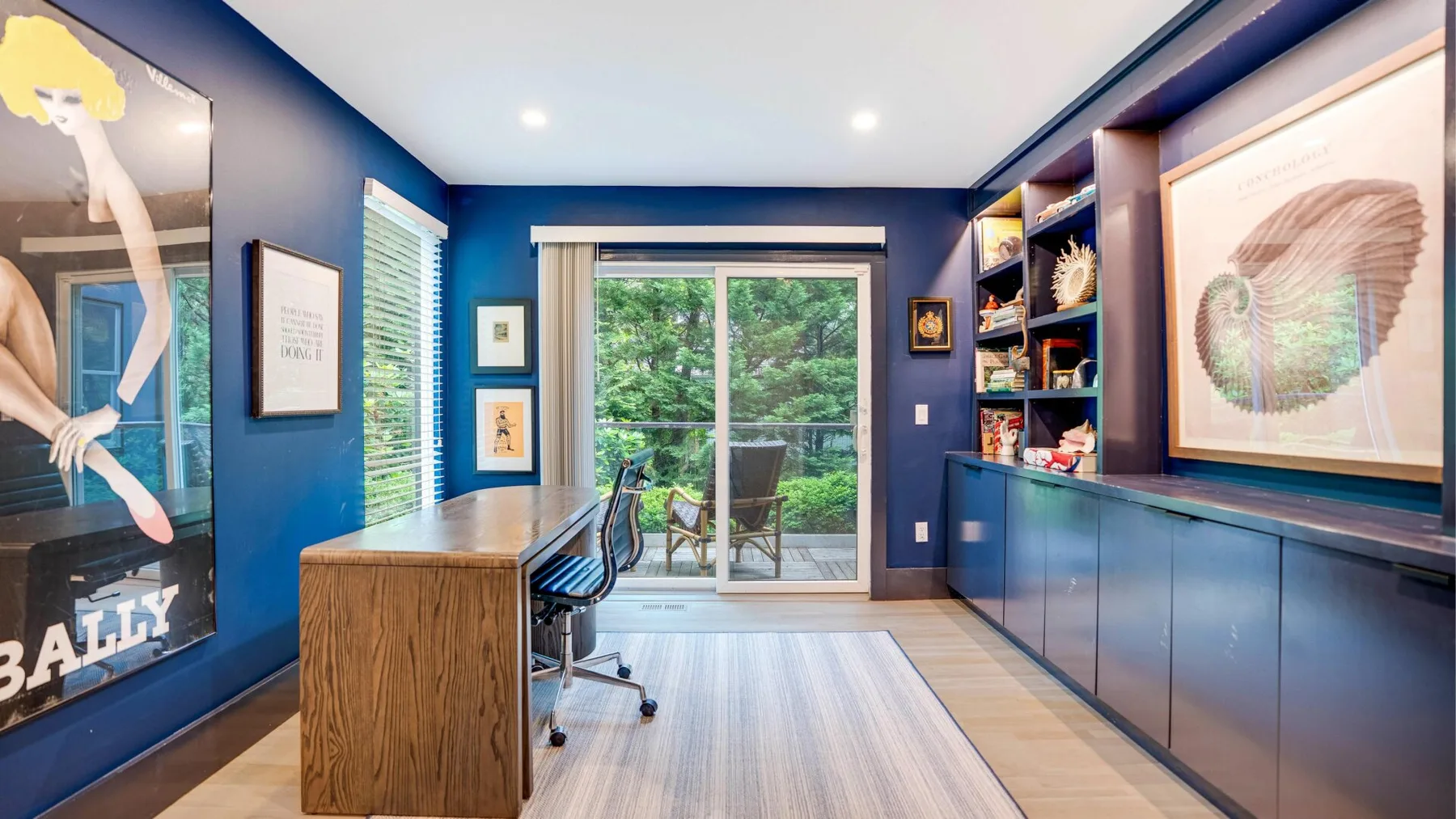 A bright blue office with a wood desk and sliding glass doors opening onto greenery.