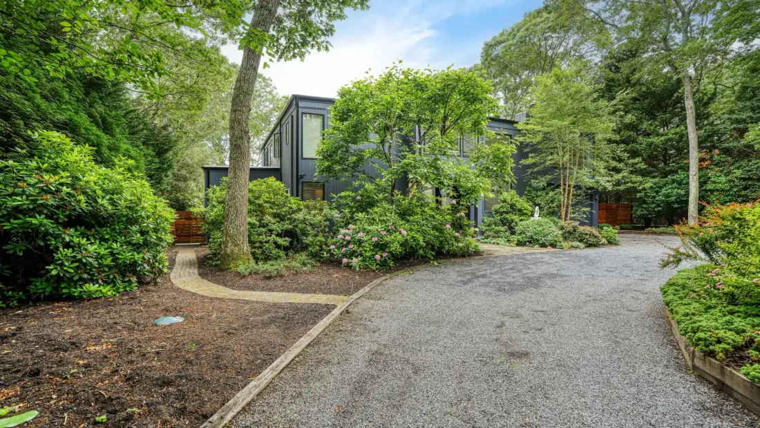 A modern building is partly visible behind trees beside a curving gravel driveway.