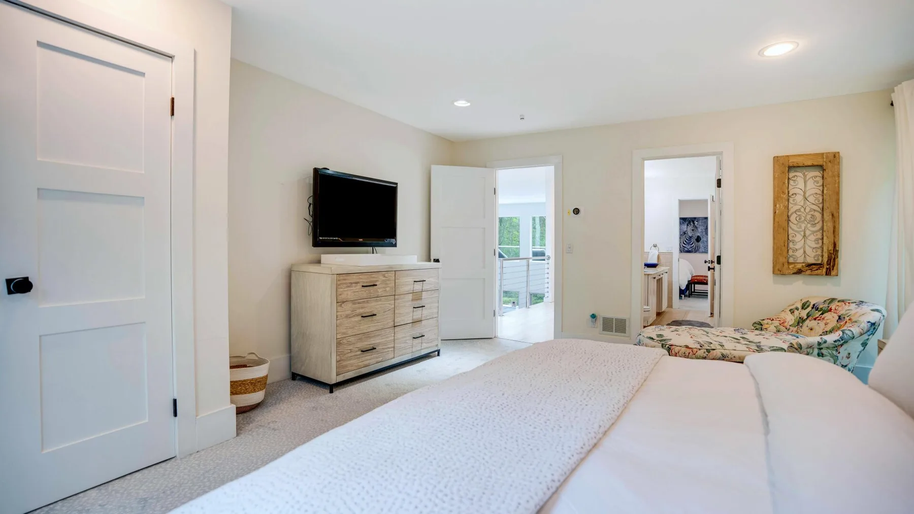 A bright bedroom with a bed, dresser, and television.