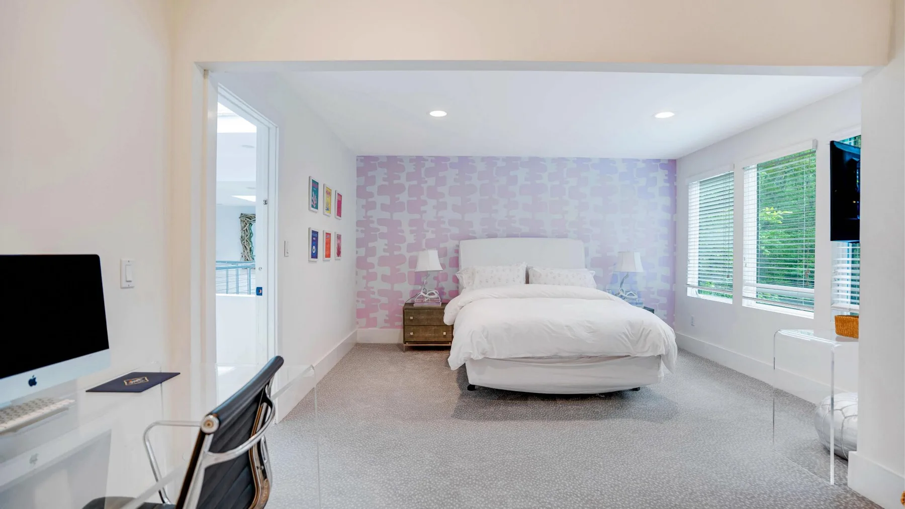 A bright bedroom with a white bed, patterned wallpaper, and windows.