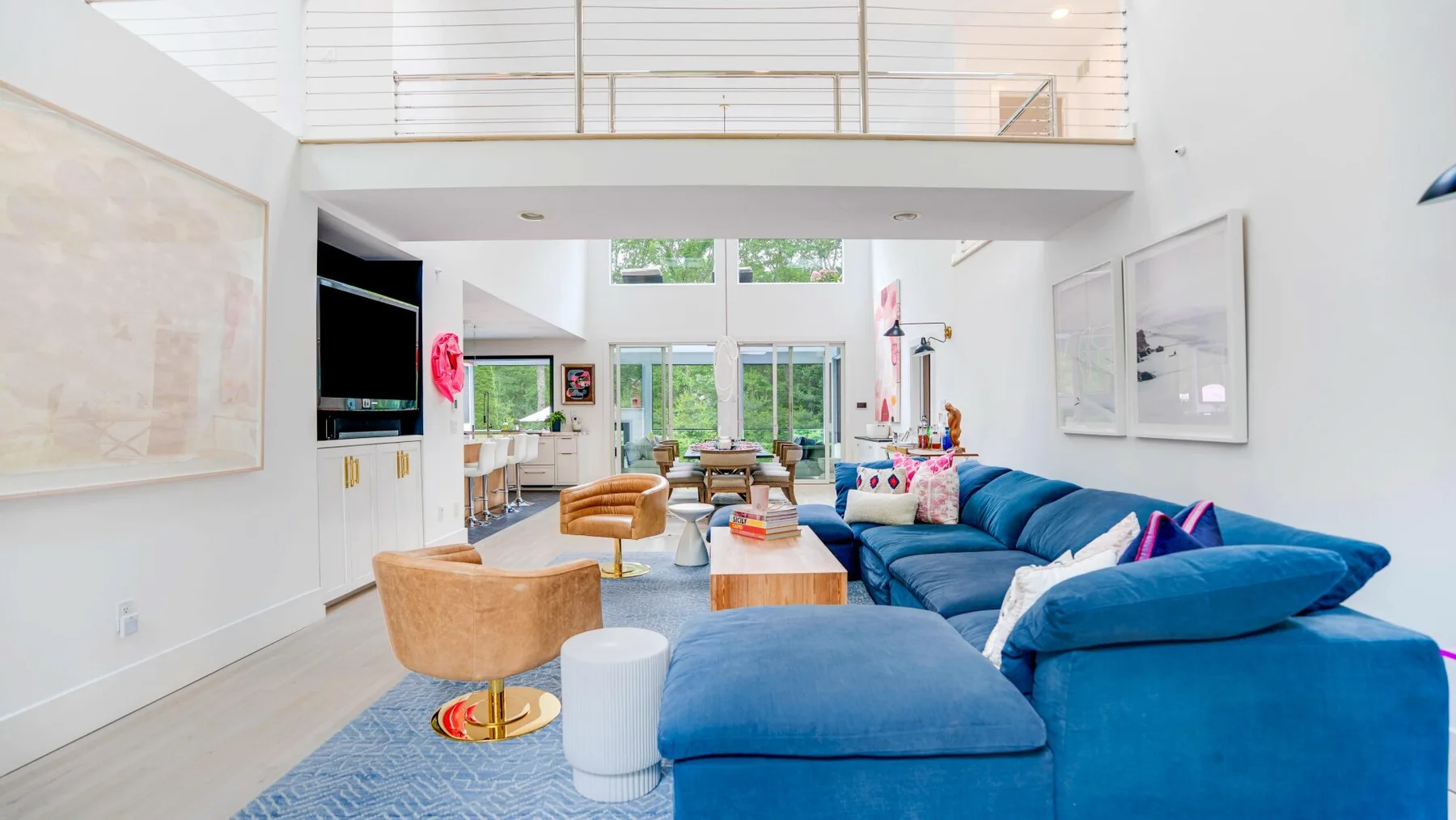 A bright living room with blue seating, a coffee table, and an upper-level railing.