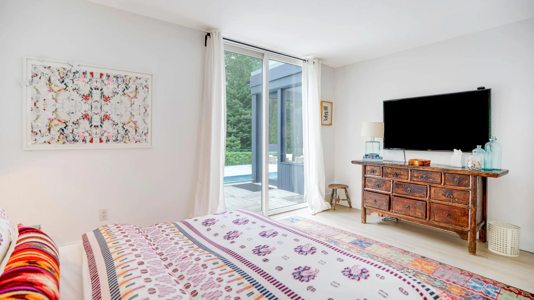 A bright bedroom with patterned bedding and a television on a wooden dresser.
