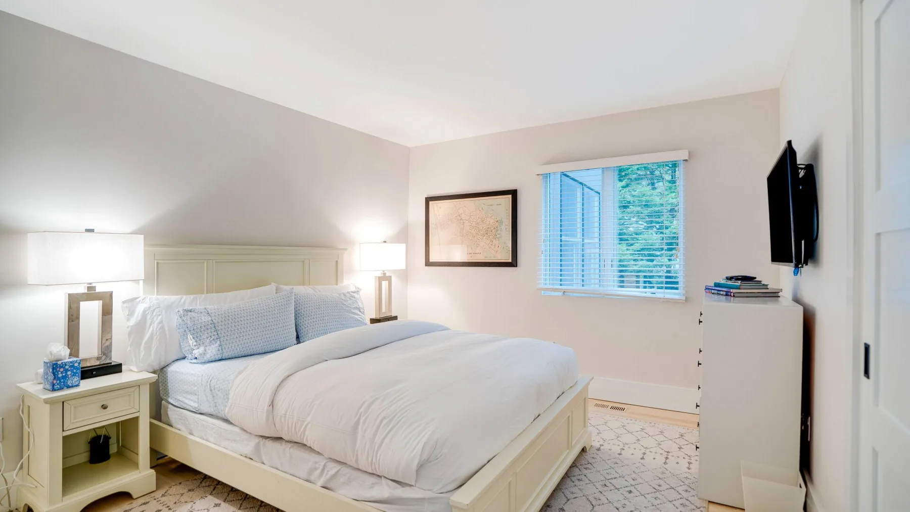 A bright bedroom with a neatly made bed and a window with blue blinds.
