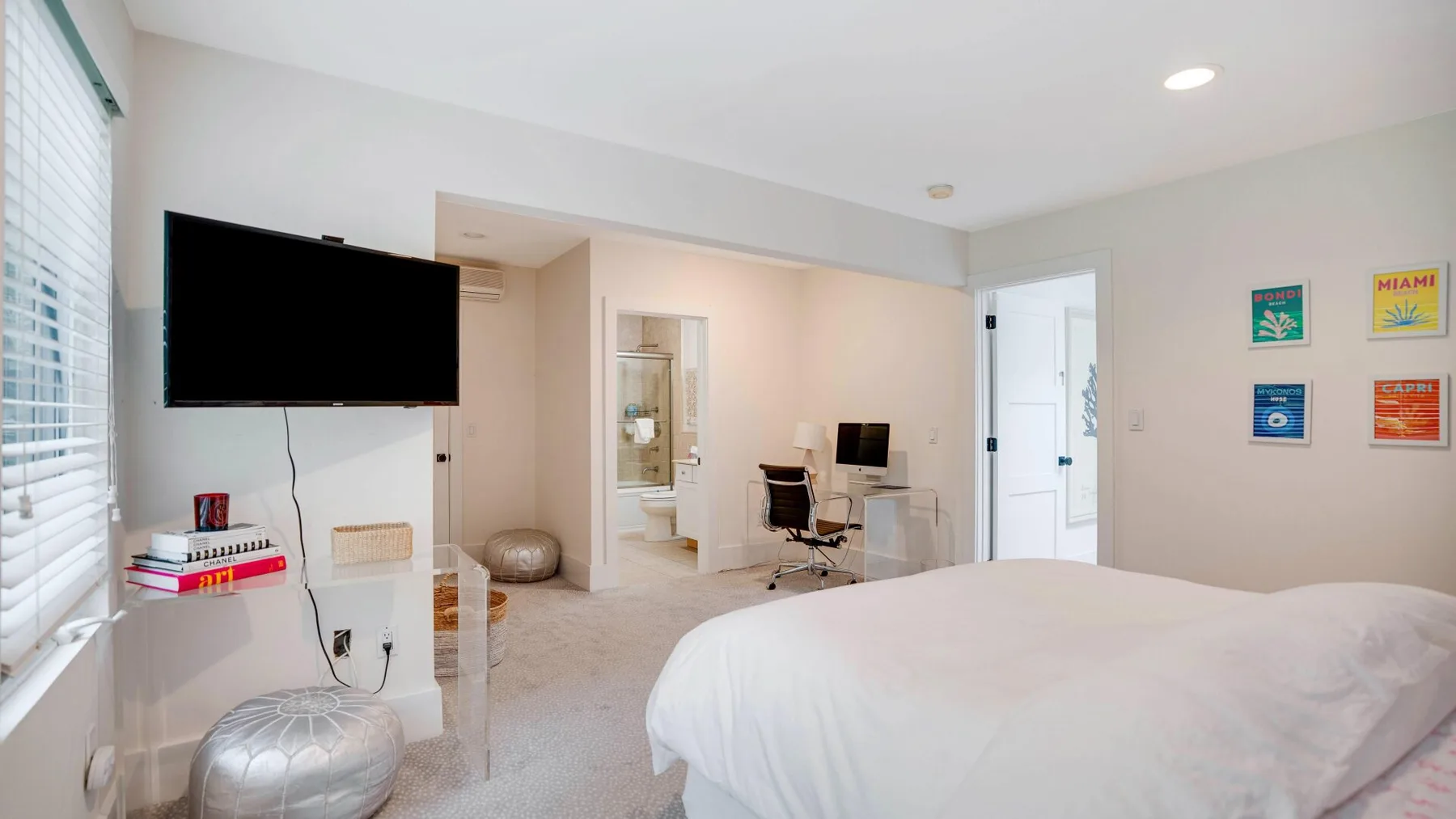 A bright bedroom with a bed, wall-mounted television, and small desk area.